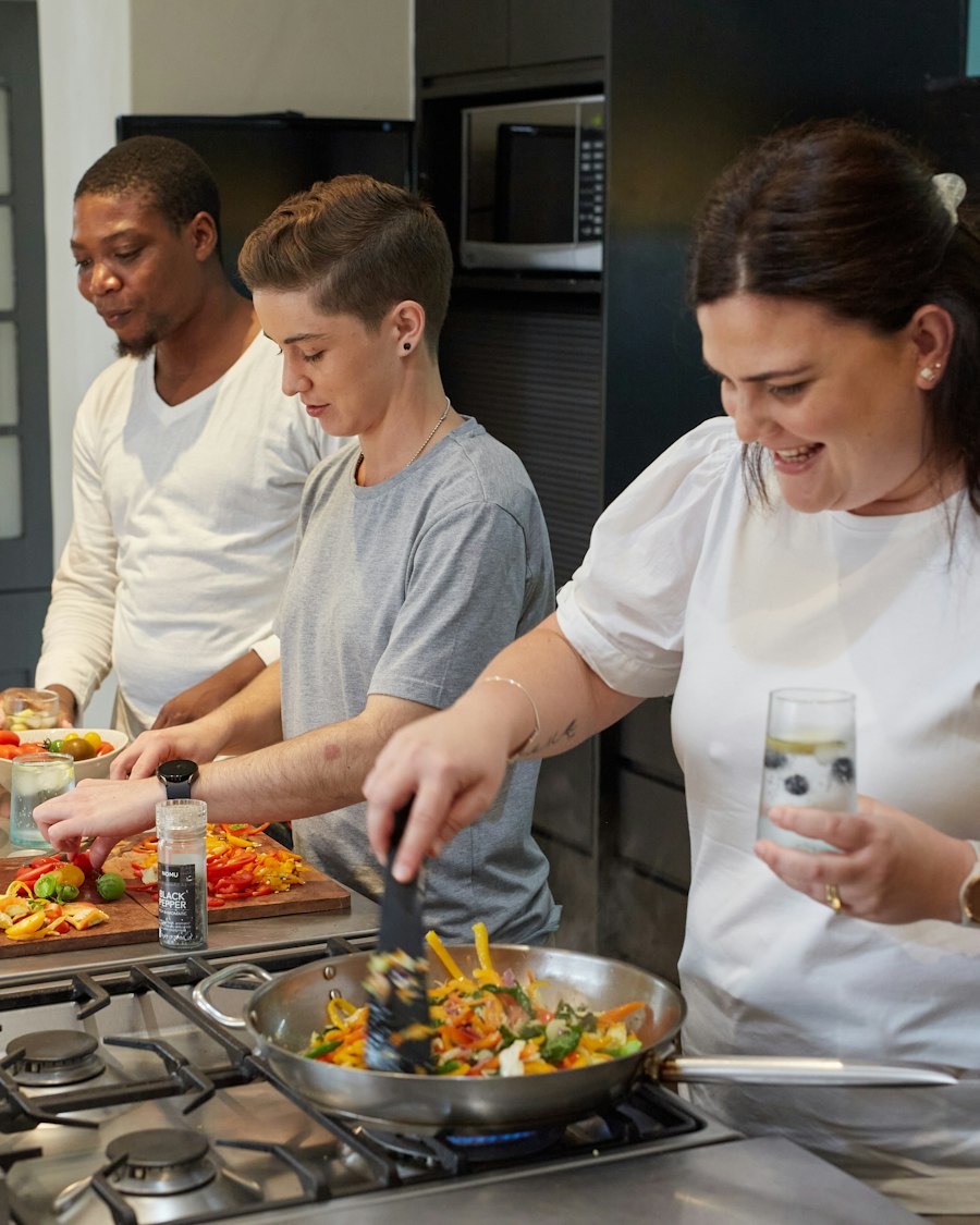 Three people cooking side by side at a stove in a class kitchen