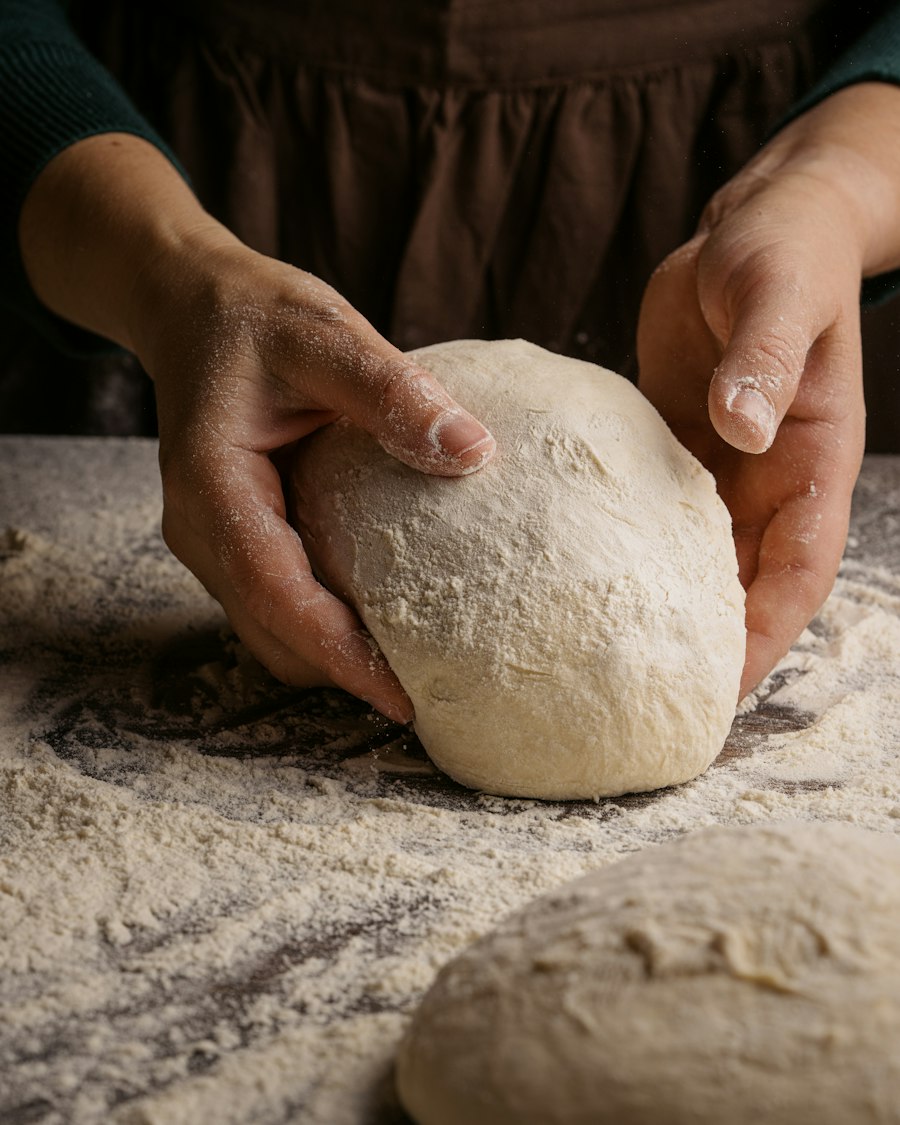 Two floured hands shaping a round of dough on a wooden bench