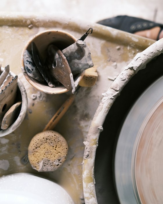 A pottery wheel spinning beside cups of trimming tools and a sponge