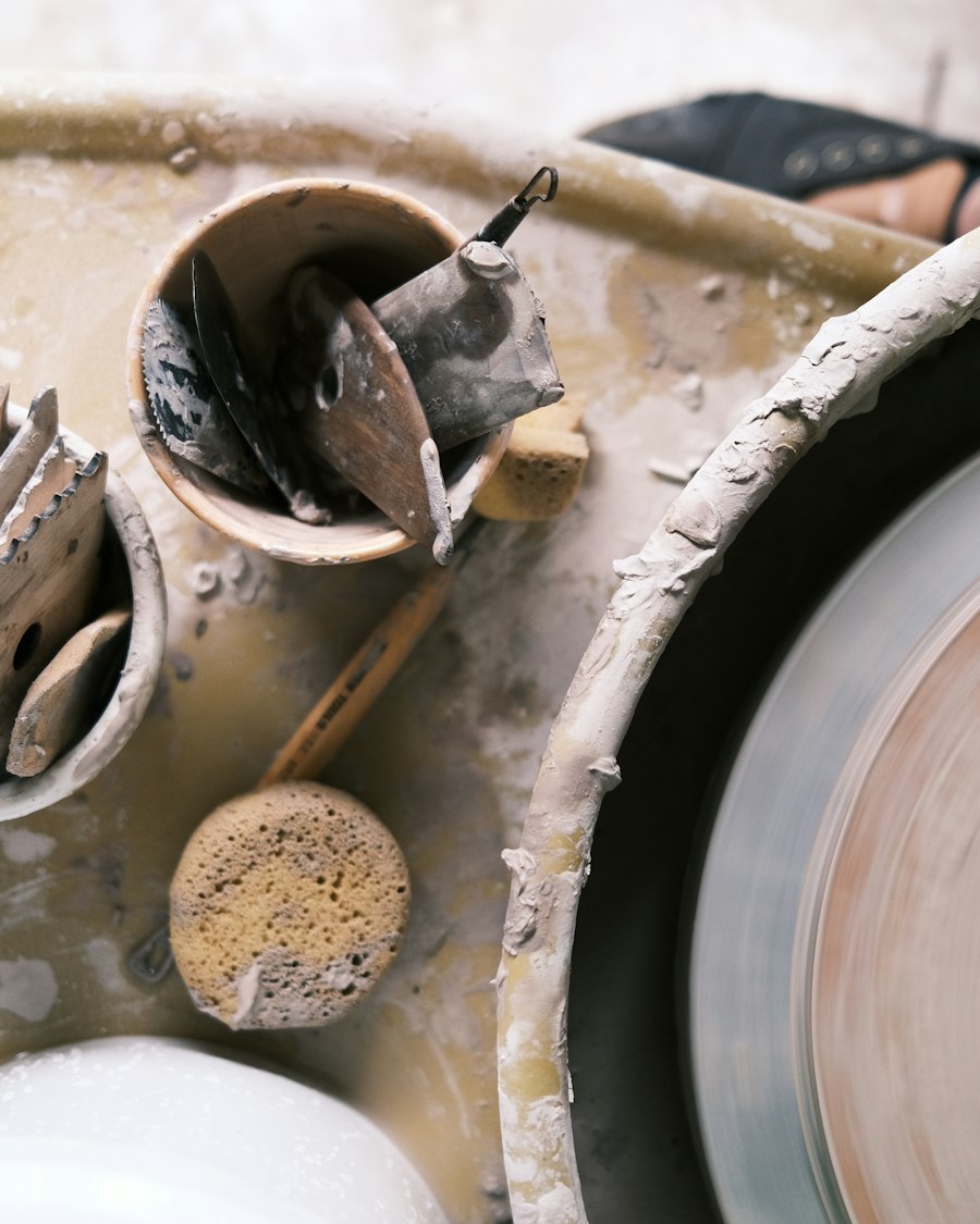 A pottery wheel spinning beside cups of trimming tools and a sponge